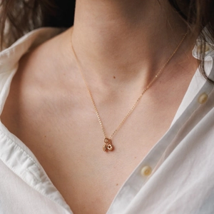 Collana minimalista dorata con piccoli ciondoli ad ape e anello su collo femminile