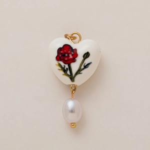Detail of vintage heart pendant with red poppy pattern and dangling baroque pearl