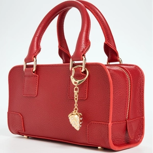 Detail of red pebbled leather handbag featuring a crystal strawberry charm and gold zipper