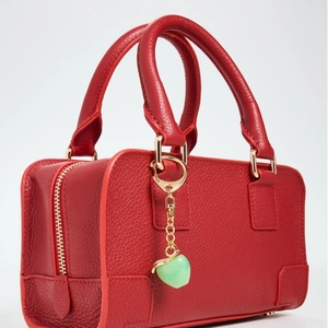 Macro detail of red litchi leather handbag with golden zipper and heart charm