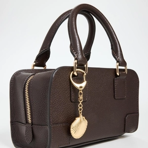 Detail of dark brown pebble leather Boston bag with gold shell charm and logo embossing