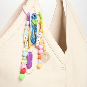 Detail of colorful beaded bag charm with DM ME blocks and woven rope on beige leather bag