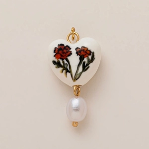 Macro shot of white heart ceramic pendant with red flower print and teardrop pearl