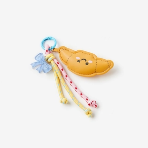 Detailed view of croissant charm with blue ribbon and rainbow woven ropes key accessory