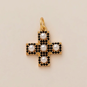 Détail d'un pendentif croix vintage doré avec perles blanches et pierres noires