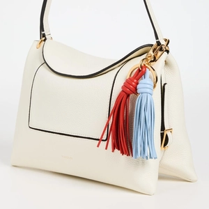 Detail of cream-colored pebbled leather handbag with blue and red fringe charms