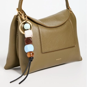 Detail of olive green leather handbag with colorful beaded tassel and gold logo