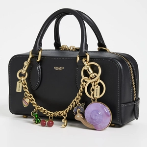 Black leather Boston bag with golden Coach logo and colorful novelty charms on handles