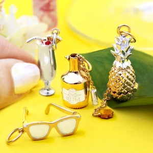 Tropical gold and silver pendant set with rum bottle pineapple and sunglasses on yellow background