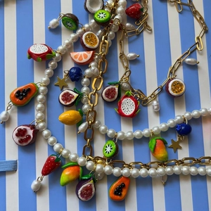 Colorful fruit pendant necklace set with faux pearls and golden chains on blue background
