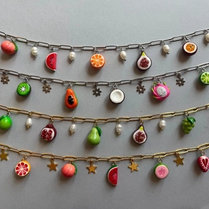 Detailed close-up of mixed fruit pendants with colorful enamel charms on gold and silver chains
