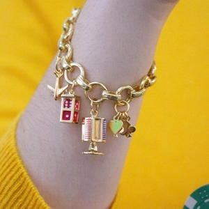 Detail of gold chunky chain bracelet with dice and airplane charms on wrist