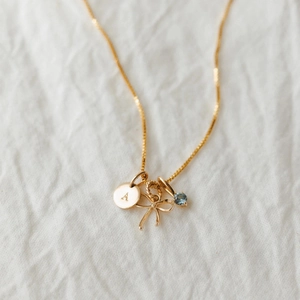 Collana d'oro con ciondolo a lettera A, pietra preziosa blu e fiocchetto dorato