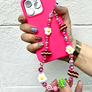 Macro detail of handmade beaded phone strap with fried egg, bacon, and smiley charms
