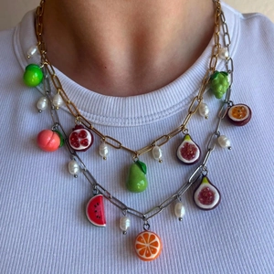 Close-up of layered gold and silver chains with colorful fruit charms and pearls