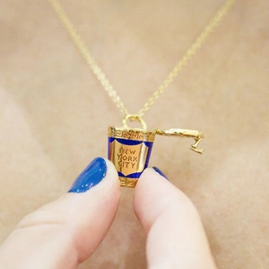 Macro detail of gold necklace pendant featuring a blue New York City coffee cup design