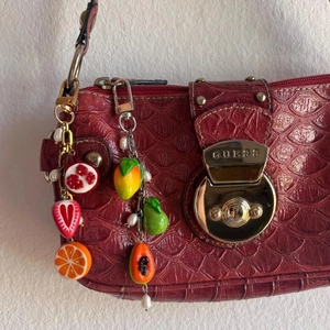 Detail of colorful resin fruit pendants with mini pearls and lobster clasp on red handbag