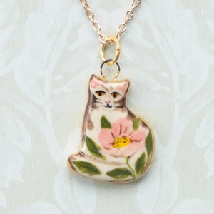Dettaglio del ciondolo a forma di gatto in ceramica bianca con fiori e catena in oro 18K