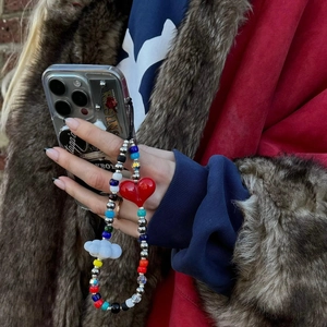 Detail of beaded phone strap with red heart and white cloud charms held by a person