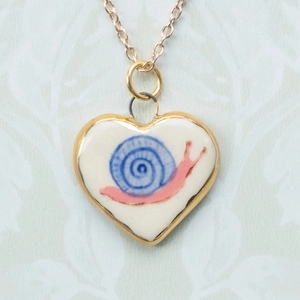 Dettaglio pendente a cuore crema con motivo lumaca blu su catena in oro elegante
