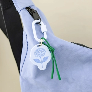 Nahaufnahme eines weißen Blumen-Taschenanhängers mit Hortensienmuster und Kordel