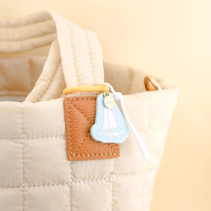 Detailaufnahme der beigen Stepptasche mit blauem Segelboot-Anhänger und Gold-Anhänger