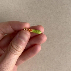 Gros plan du pendentif en cuivre émaillé avec logo RAW et boucle dorée