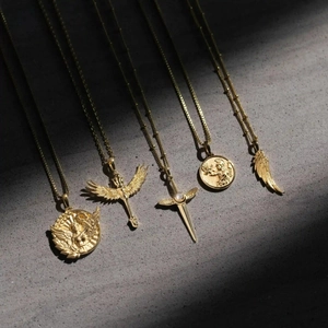 Makroansicht goldener Vintage-Halsketten mit geprägten Engelsflügeln und Schwert-Details