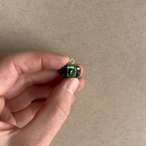 Vue rapprochée d'un mini pendentif appareil photo noir et vert tenu par les doigts