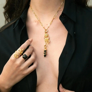 Detail einer goldenen Büroklammer-Halskette mit Schlangenanhängern und passenden Ringen am Model