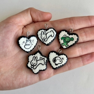 Macro shot of five handmade heart charms featuring cartoon characters on a hand
