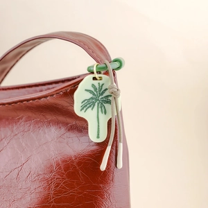 Detail einer Vintage rotbraunen Lederhandtasche mit grünem Palmenanhänger als Zubehör