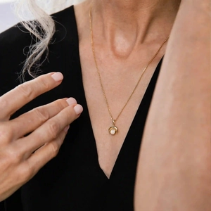 Detail einer minimalistischen Goldkette mit weißem Edelsteinanhänger an einem Frauenmodel