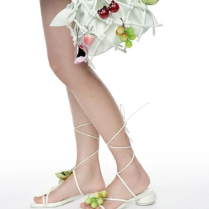 Detalle de sandalias blancas con cordones y bolso trenzado con colgantes de frutas