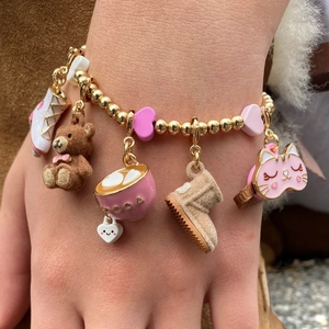 Close-up of golden beaded bracelet with bear, cocoa cup, and ice skate charms on wrist
