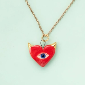 Red heart necklace with blue evil eye detail and gold accents on a minimal background