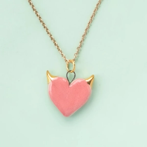 Detail of pink devil heart necklace with gold horns on a mint green background