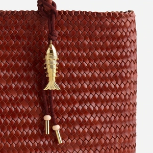 Detail of woven burgundy leather bag featuring a gold fish charm and delicate pink bead