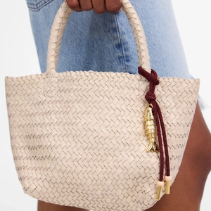 Detail of beige woven handbag with fish metal pendant and red cord charm keychain