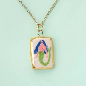 Detail shot of a handmade mermaid pendant with a gold chain on a mint green background