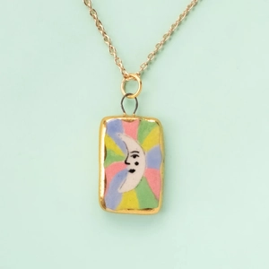 Macro detail of a rectangular gold pendant with a rainbow enamel crescent moon design