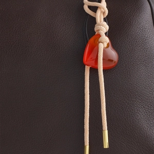Macro detail of red heart pendant with woven cord on a lychee grain leather handbag