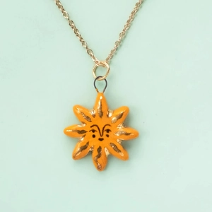 Close-up of an orange octagonal sun pendant necklace with a minimalist smiley face art
