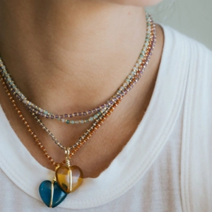 Gelaagde kralenketting met kleurrijke kralen en dubbele hartvormige hangers op wit hemd