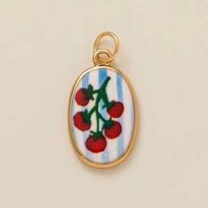 Macro detail of oval gold pendant featuring hand-painted red tomato on blue striped base