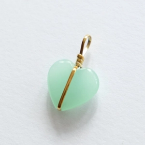 Detail van hartvormige groene stenen hanger met gouden draadwikkeling op witte basis