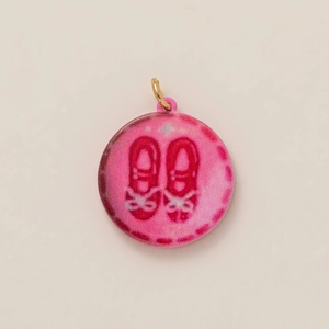 Detailed view of a pink round charm with red ballet shoes and golden metal loop