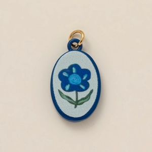 Macro detail of oval ceramic floral pendant with blue flower and gold ring