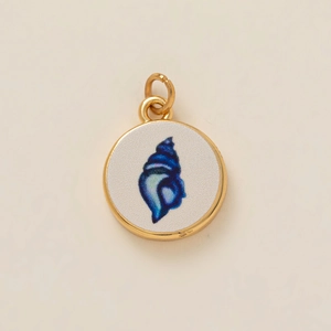 Detalle de un colgante circular dorado con un diseño de caracola azul oscuro en cerámica