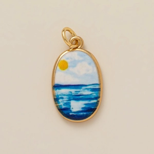 Detailed close-up of a seaside enamel oval pendant with sun and waves in gold plating